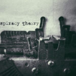 Image of a typewriter typing the words "conspiracy theory" on a piece of paper.